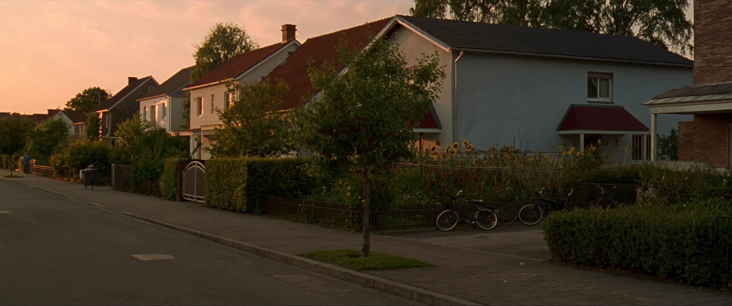 Illustration: Eine ruhige deutsche Kleinstadtstraße am Sommerabend mit Vorgärten und Schrebergärten.
